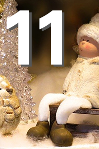 Weihnachtliche Szene: eine sitzende kleine Figur in weißer Winterkleidung und Mütze auf einer Bank, neben einer glitzernden Kristall-Weihnachtsbaum-Dekoration auf schneebedecktem Untergrund.