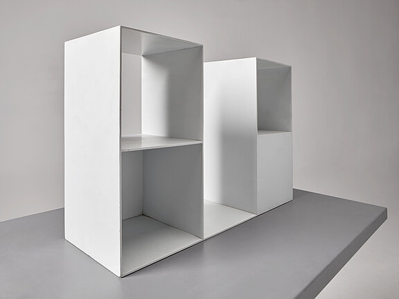 Zwei weiße, minimalistische offene Regalmodule mit mehreren quadratischen und rechteckigen Fächern stehen nebeneinander auf einer grauen Oberfläche vor neutralem Hintergrund.