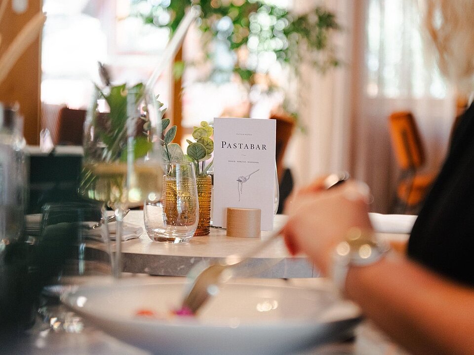 Detailaufnahme von einem Tisch mit zwei Personen, die ein Nudelgericht essen.