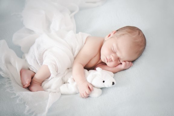 Ein Baby schläft und hält einen Teddybär unter dem Arm. 
