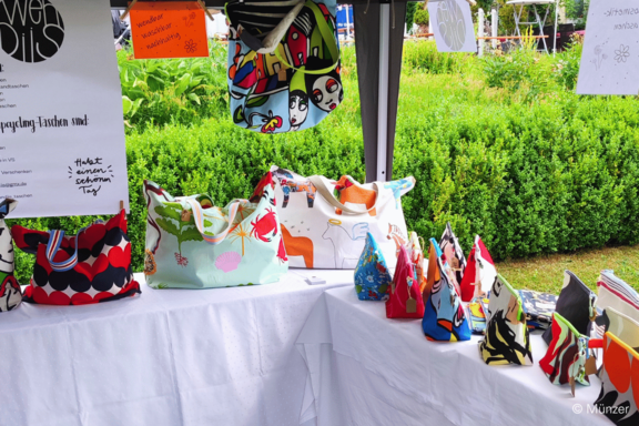 Marktstand im Freien mit bunten, gemusterten Stofftaschen und kleinen Reißverschlusstäschchen, dekorativ auf weißen Tüchern präsentiert.