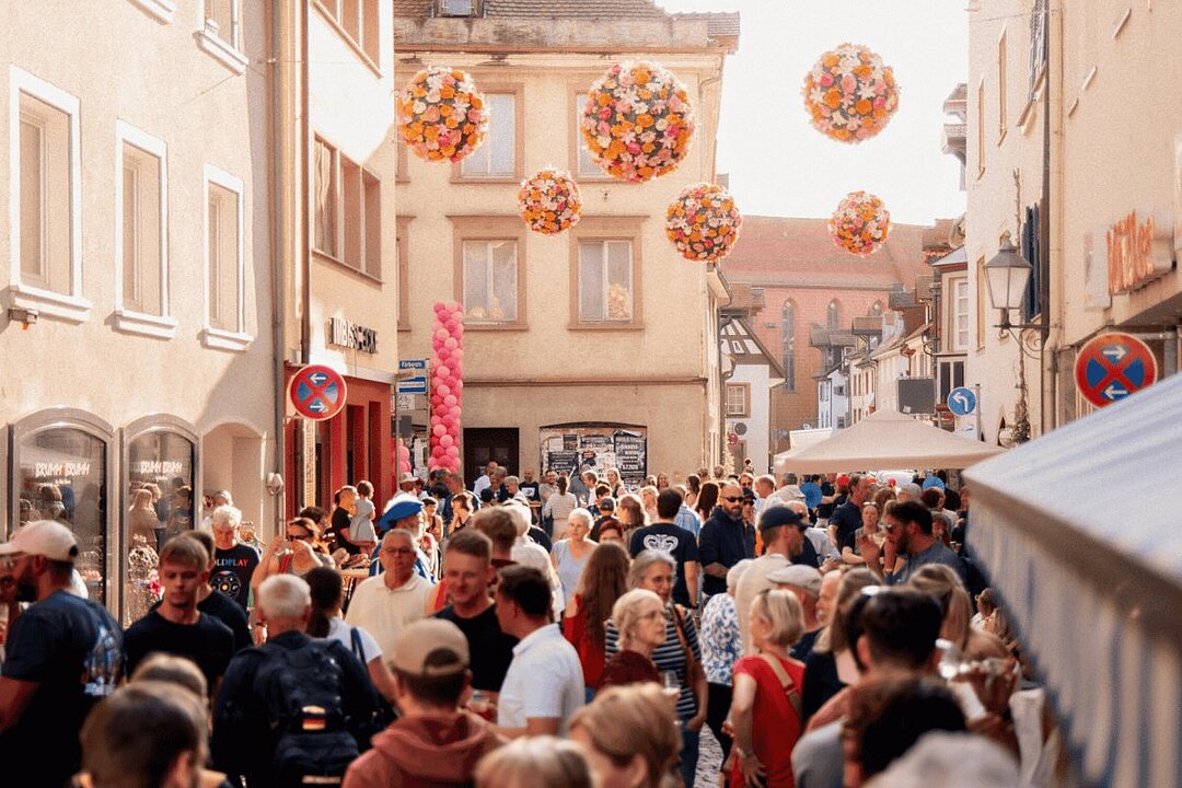 Große Menschenmenge in einer engen Gasse mit Laternen und Schildern, viele tragen Masken. (KI generiert)