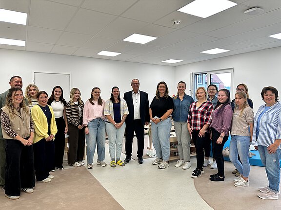 Gruppe von etwa sechzehn Erwachsenen, überwiegend Frauen, die in einem hellen Besprechungsraum in einer Reihe stehen und lächelnd in die Kamera blicken.