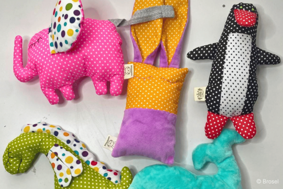 Mehrere bunte, gepunktete Stofftiere: ein pinker Elefant, ein schwarz-weiß gepunkteter Pinguin, ein grün-weiß gepunktetes Seepferdchen, ein türkisfarbener Wal und ein orange-lila Stoffbeutel mit Ohren.