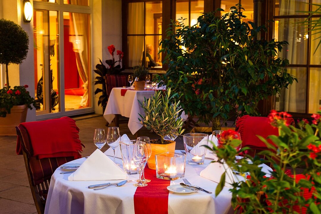 Restauranttisch mit zwei Personen, Gläsern, Blumen und Kerzen in warmem Licht. (KI generiert)
