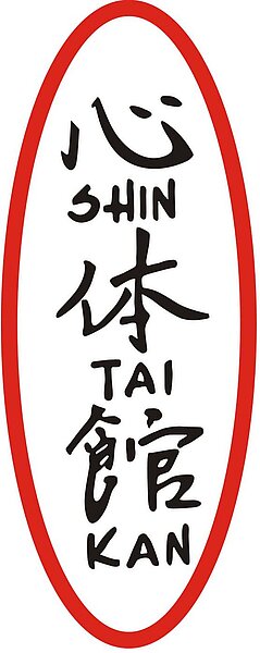 Rotes ovales Schild mit vertikal angeordneten japanischen Schriftzeichen 心, 体, 館 und den lateinischen Umschriften "SHIN", "TAI", "KAN".