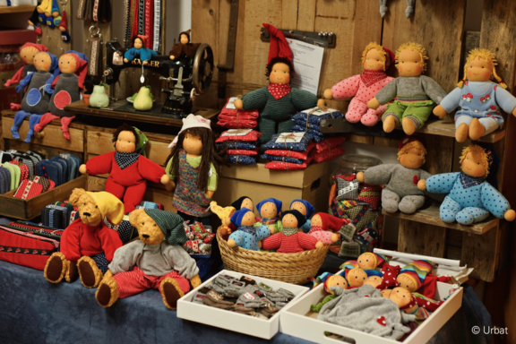 Marktstand mit handgefertigten Stoffpuppen und Plüschbären in bunten Kleidern, arrangiert in Körben, Kisten und auf Holzbrettern.