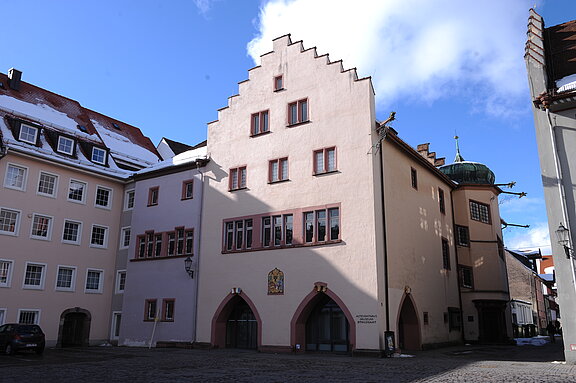 Altes Rathaus VS-Villingen Historisches hellrosa Giebelhaus mit Treppengiebel, Wappen über Rundbögen im Erdgeschoss, an gepflastertem Marktplatz unter blauem Himmel.