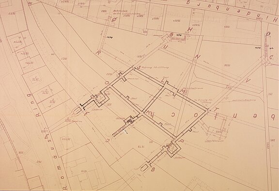 Lageplan eines Gebäudekomplexes: Grundrisse dreier verbundener rechteckiger Baukörper, Verbindungswände, umgebende Parzellen, Straßenverläufe und Maßangaben.