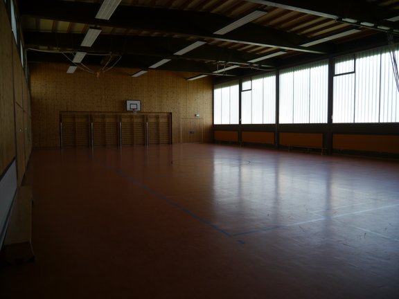 Spielfeld einer Turnhalle mit Basketballkörben und einer Sprossenwand 