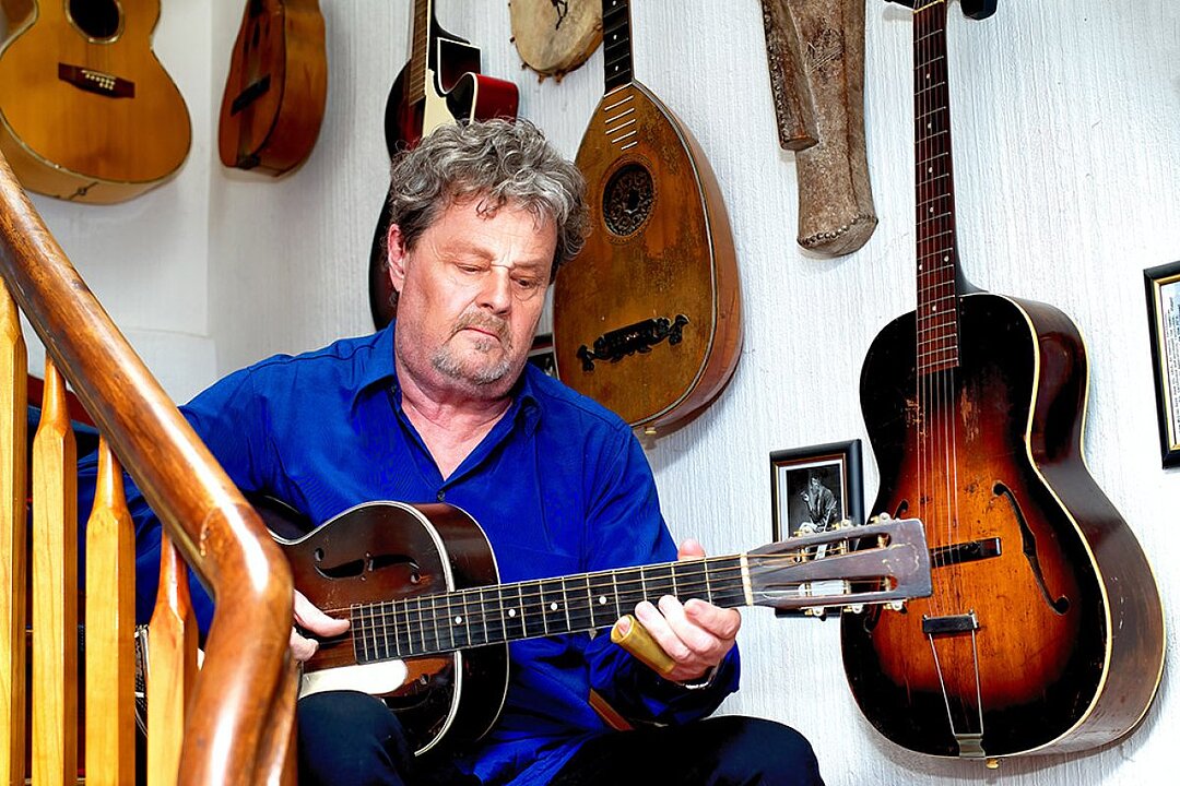 Mann in blauem Hemd spielt auf einer Gitarre in einem Musikladen. (KI generiert)