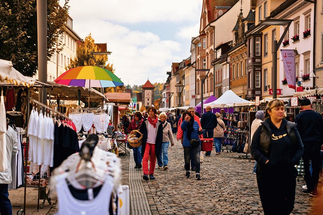 Bunte Regenschirme und Menschen in einer belebten Altstadtgasse bei Regen. (KI generiert)