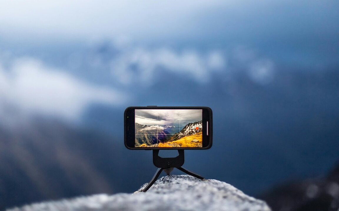 Hand hält Smartphone mit Foto eines Gletschers vor blauem Himmel. (KI generiert)