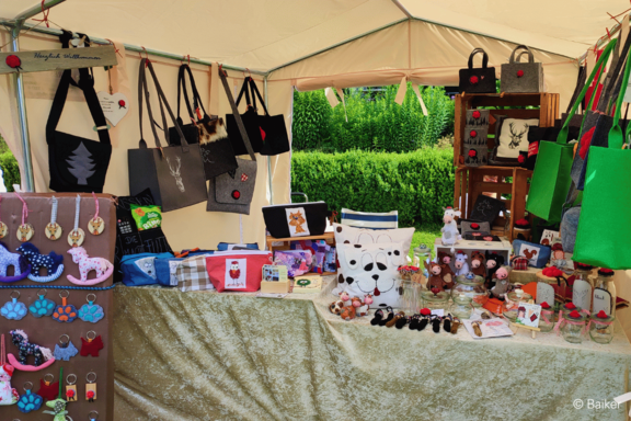 Marktstand mit handgefertigten Artikeln: Filz- und Stofftaschen, Kissen, Stofftiere, Schlüsselanhänger und kleine Dekorationen auf Tischen und Regalen unter einem Zelt.
