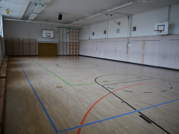 Turnhalle mit Parkettboden, mehreren Basketballkörben und Sprossenwänden an der Wand 