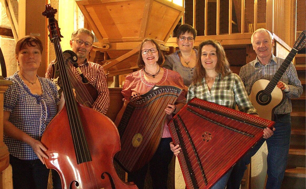 Fünf Personen halten Gitarren in einem Raum mit Holzvertäfelung und lachen. (KI generiert)