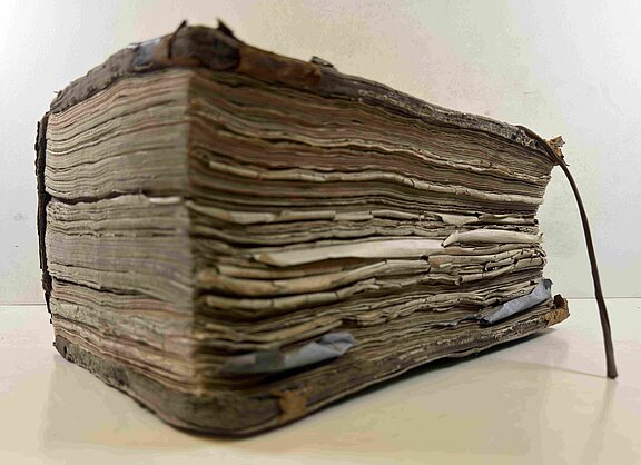 Altes, sehr dickes Buch mit vergilbten, unregelmäßig gewellten Seiten, abgenutztem Einband und einem Lederband-Lesezeichen.
