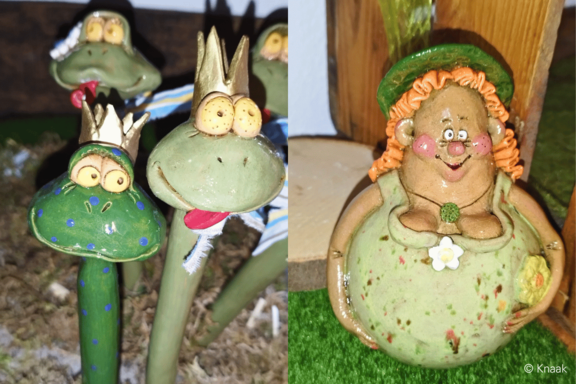 Keramikgartenfiguren: drei grün lackierte Froschköpfe mit goldenen Kronen und großen Augen links; rechts eine rundliche, lachende Frauengestalt mit orangenem Zopf, grünem Hut und Blumenmotiv auf dem Bauch.