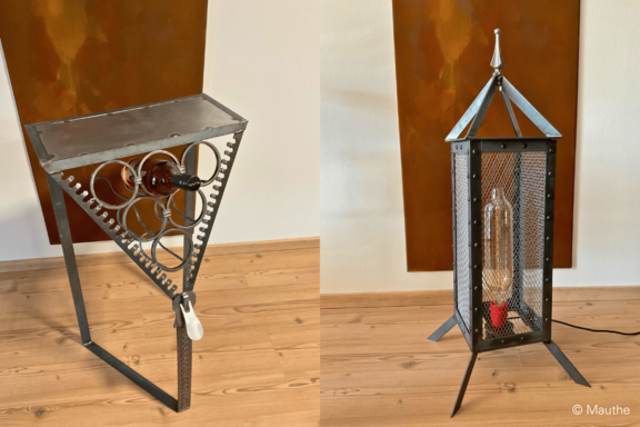 Zwei industrielle Metalllampen: links ein dreieckiger Tisch mit Zahnrädern und eingebauter Glasflasche, rechts eine hohe Laterne mit Gittergehäuse und sichtbarer Glühlampe.