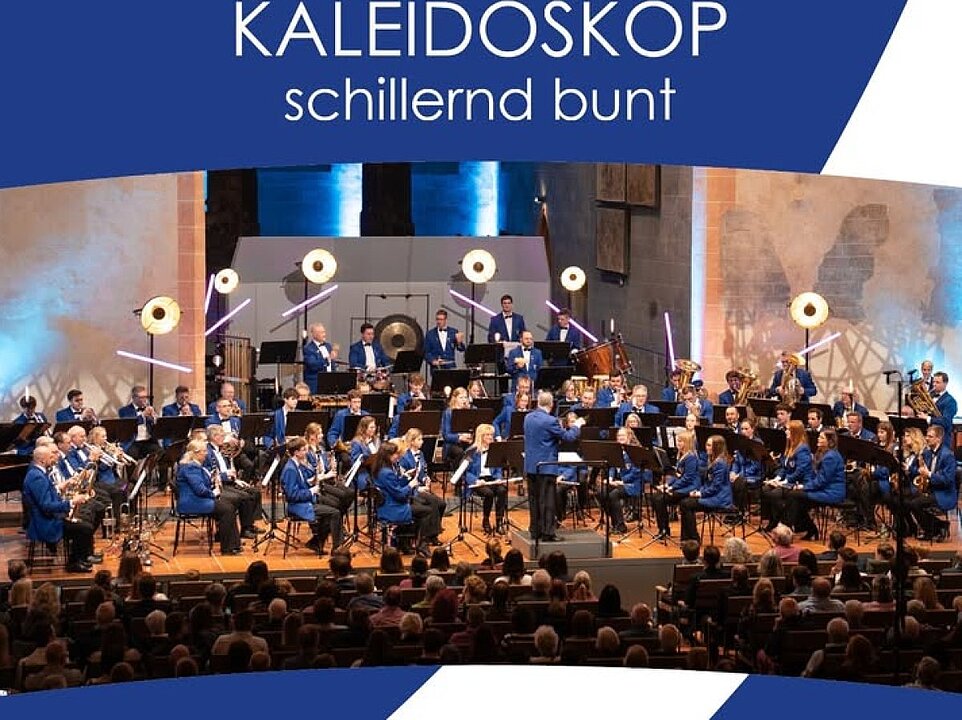 Großes Orchester spielt vor Publikum auf einer Bühne mit bunter Lichtshow. (KI generiert)
