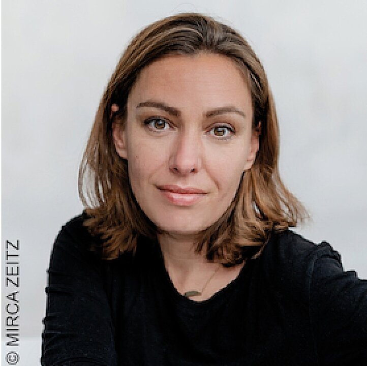 Porträt einer lächelnden Frau mit braunen Haaren und dunklem Blazer. (KI generiert)