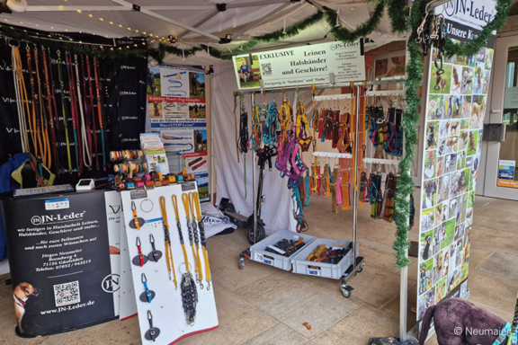 Marktstand mit vielen bunten Hundeleinen, Halsbändern, Geschirren und Lederzubehör, aufgehängt und auf Tischen ausgestellt.