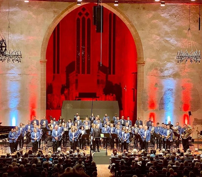 Großes Orchester spielt vor Publikum in prächtigem Saal mit rotem Vorhang. (KI generiert)