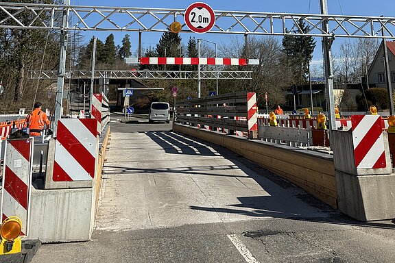 Peterzeller Brücke Engstelle einer Baustelle: ein einspuriger Fahrstreifen mit roten-weißen Absperrungen, Höhenbeschränkungsschild 2,0 m über dem Durchgang, Bauarbeiter in Warnkleidung und ein Auto, das durchfährt.