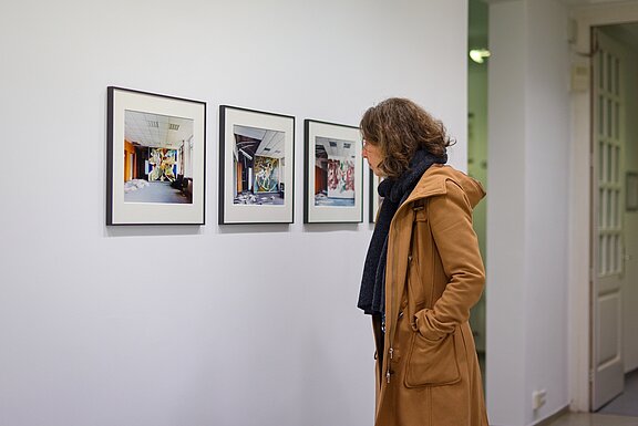 Restwert Ausstellung Eine Frau betrachtet drei Bilder, welche eingerahmt an der Wand hängen.