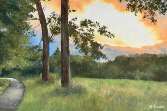 Landschaft mit zwei markanten Bäumen am linken Bildrand, schmalem geschwungenem Weg, weiten Wiesen und entferntem Waldrand vor einem orange-rosa beleuchteten Sonnenuntergangshimmel.