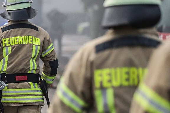 Mehrere Feuerwehrleute von hinten an einer Einsatzstelle mit einem Fahrzeug.