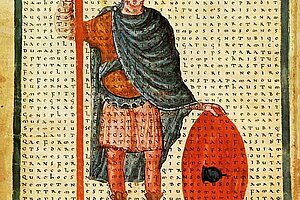 Illuminierte Miniatur einer stehenden Figur in Tunika und Umhang, die einen langen Stab mit Kreuz und einen großen runden Schild hält; Hintergrund aus engbedrucktem Buchstabentext.