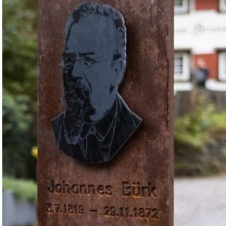 Bronzetafel mit Porträt von Johannes Bürk, Geburts- und Sterbedatum eingraviert. (KI generiert)