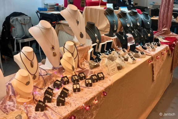 Verkaufsstand mit Schmuck: Halsketten auf weißen und schwarzen Büsten, Ringe und Ohrringe in Schachteln und auf Polstern, auf einem dekorativen Tisch drapiert.