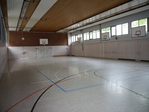 Spielfeld einer Turnhalle mit mehreren Basketballkörben sowie Handballtoren 