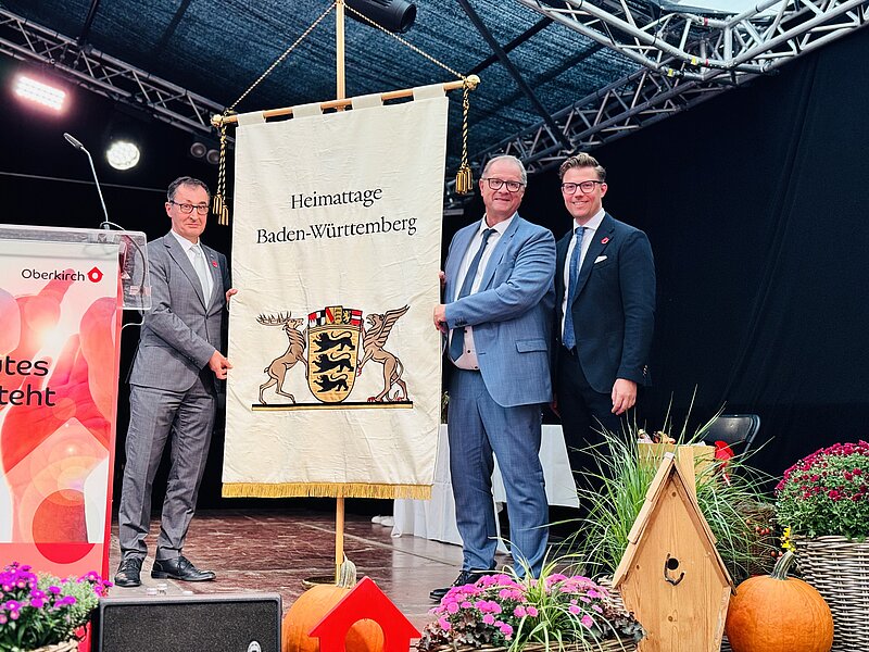 Ministerpräsident Cem Özdemir (links) übergab die Heimattagefahne feierlich bei den Landesfesttagen in Oberkirch an Oberbürgermeister Jürgen Roth (Mitte). Gregor Bühler, Oberbürgermeister von Oberkirch (rechts), gibt den Staffelstab damit an die Stadt Villingen-Schwenningen weiter.