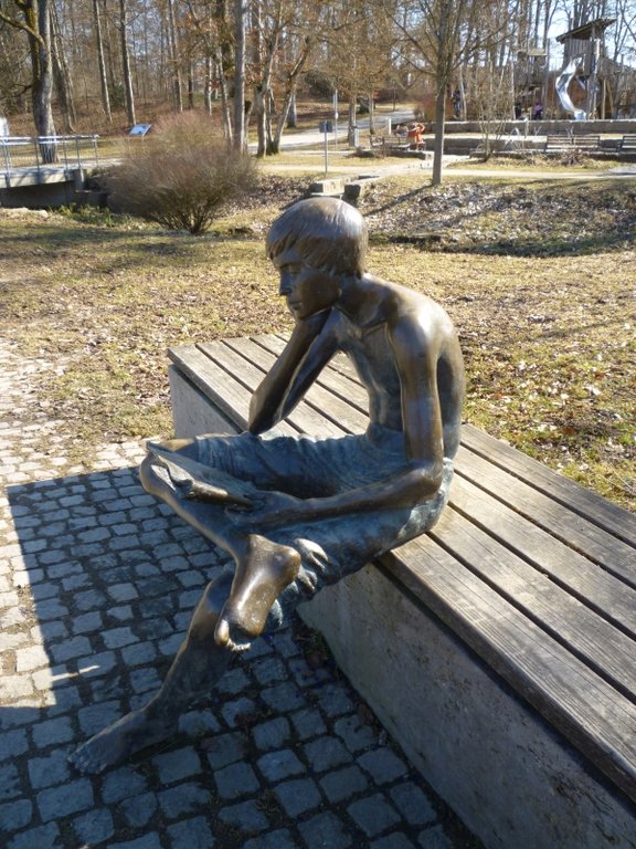 Sitzender Junge aus Bronze, der die Zeitung liest