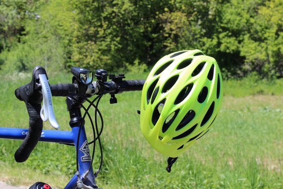 Leuchtgelber Fahrradhelm hängt am Lenker eines blauen Rennrads vor Wiese und Bäumen.