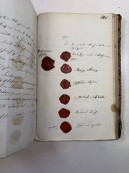 Offenes altes Manuskript: rechte Seite mit sechs roten Siegellack-Siegeln in vertikaler Reihe neben handschriftlichen Unterschriften.
