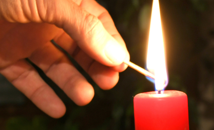 Ein Adventskranz mit vier roten Kerzen. Eine wird mit einem Streichholz angezündet.