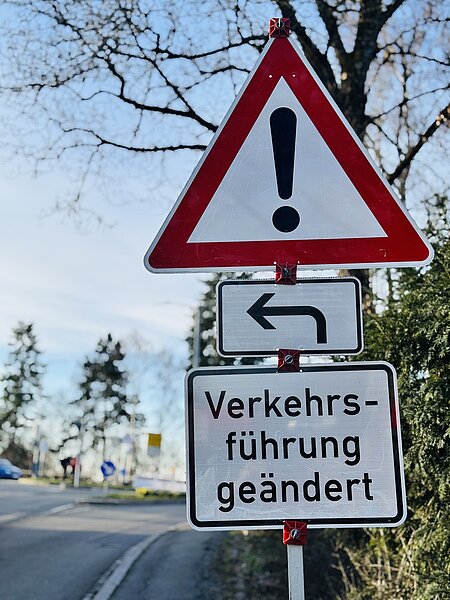 Straßenschilder: rotes Dreieck mit Ausrufezeichen, Pfeil nach links und Schild „Verkehrsführung geändert“ — Hinweis auf geänderte Verkehrsführung und linke Umleitung.