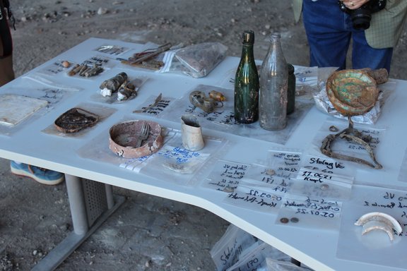 Auf einem Tisch liegen Fundstücke der archäologischen Grabungen, wie Flaschen, Essgeschirr, Knöpfe. 