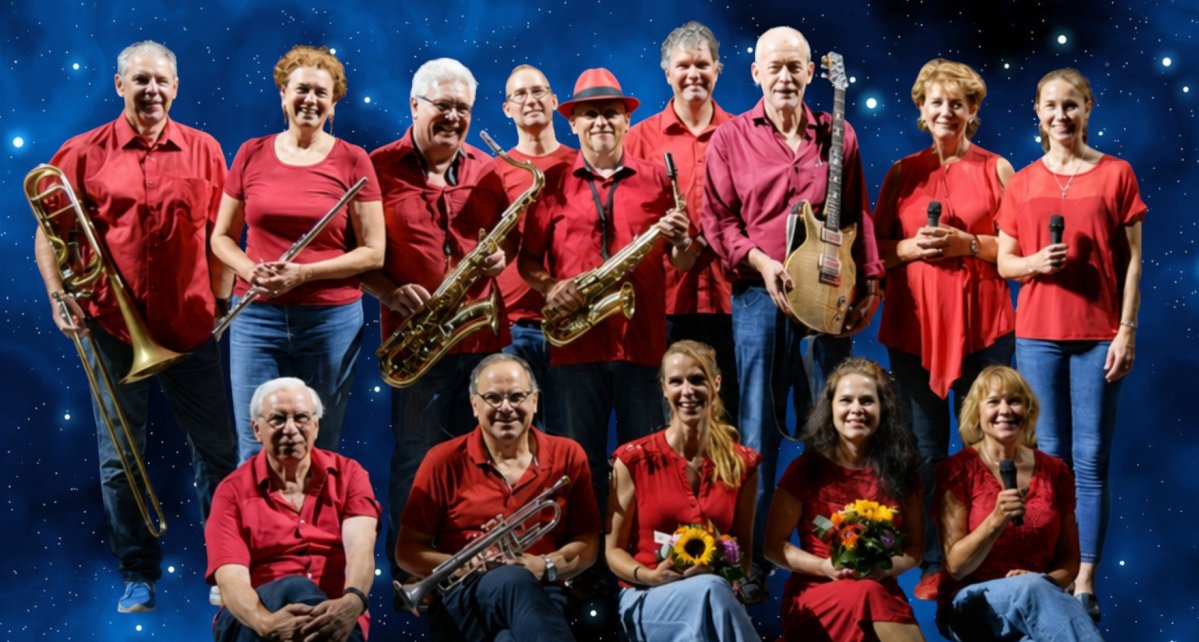Gruppe von 12 Personen in roten T-Shirts mit Instrumenten und Notenständern auf einer Bühne. (KI generiert)